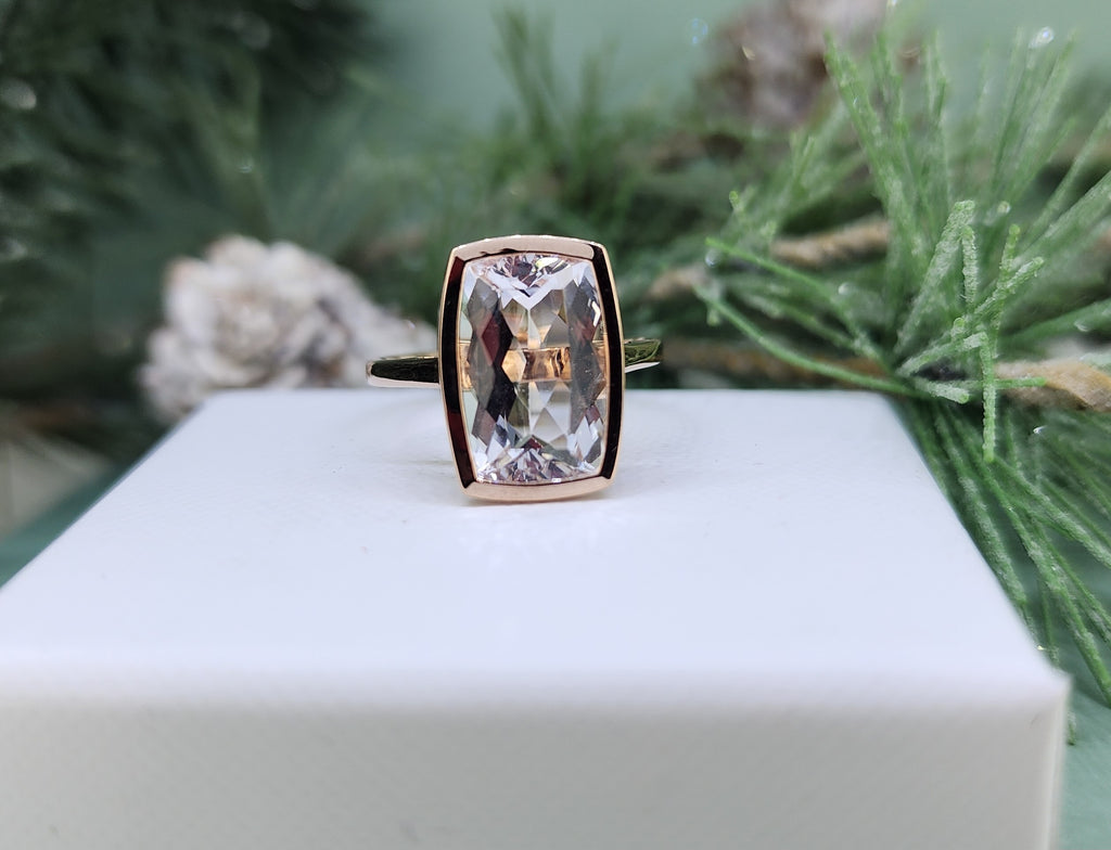  Sleek and sophisticated, this 14k rose gold ring features a striking 3.83 carat natural morganite, expertly cut to highlight its soft blush tones and luminous clarity. The elongated fancy cut is framed in a smooth rose gold bezel, creating a modern silhouette that allows the morganite’s natural beauty to take center stage. Minimal yet impactful, this ring is a timeless expression of understated luxury. The full bezel measures 15.00mm across the top and 9.00mm in width. Stunning classic!