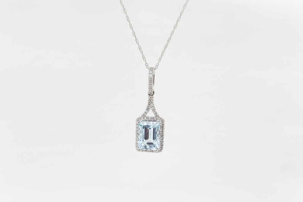 Crafted in 10k white gold this stunning pendant holds an 8x6 natural emerald cut Aquamarine surrounded .15ct carat total weight in natural mined round brilliant cut diamonds and hung from an 18 inch 1ok white gold chain with a spring ring clasp
 
