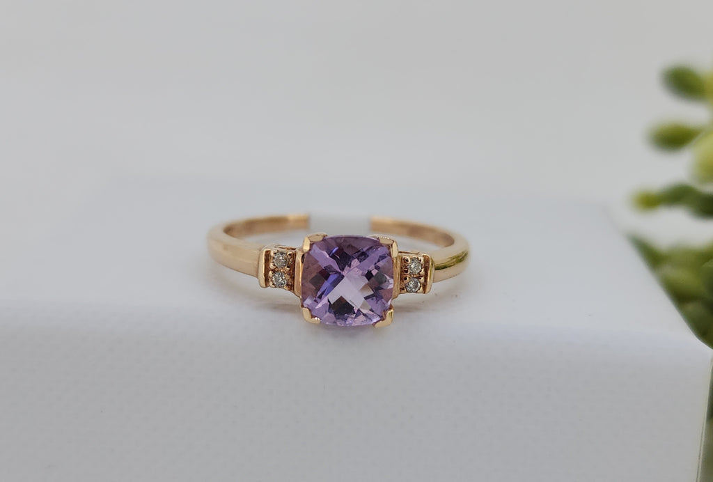 Softly radiant and beautifully balanced, this ring features a 6×6mm cushion checkerboard-cut light amethyst, admired for its gentle lavender hue and dimensional sparkle. The center stone is accented by natural mined diamonds totaling .03 carat total weight, adding a subtle touch of brilliance on each side.

Crafted in 14K rose gold, the warm setting enhances the amethyst’s delicate color. Measuring 6.02mm at the top and tapering to a slender 1.41mm shank, this ring offers a graceful profile designed for com