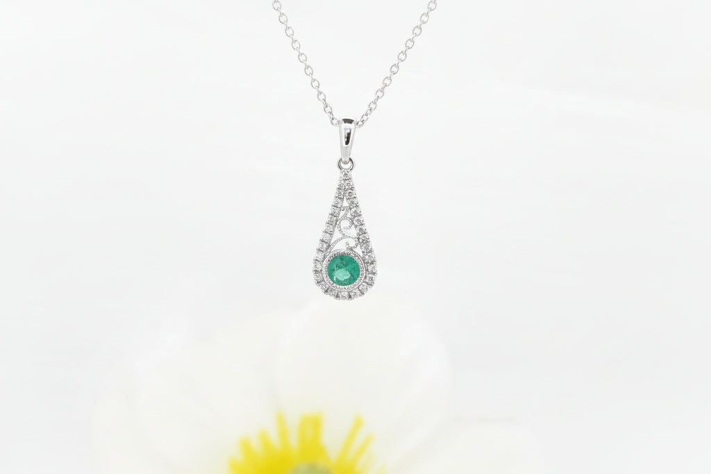 This graceful pendant is crafted in 14k white gold and features a 4.00mm round cut natural emerald at its center. The lively green emerald is accented by .15 carat total weight of natural mined diamonds, adding elegant sparkle and highlighting the pendant’s delicate openwork design.

The pendant is suspended from an 18-inch 14k white gold Singapore chain, offering a soft shimmer and comfortable everyday wear.

A timeless piece that blends classic color with refined detail.