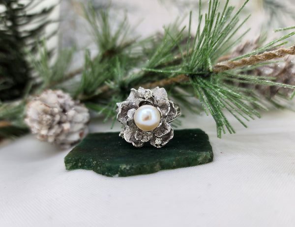 What a stunning pearl ring! This lovely pearl ring is made from 14k white gold. The gold forms delicate leaves. There are (3) three single cut diamonds and a 7.80mm single cultured pearl set amongst the petals of the ring. The brutalist design indicates this ring was probably made in the 1970's. The ring measures 21mm at the top and tapers to a 2.14mm shank

*This is an estate ring. All stones are sized by measurements only and not by scale weight