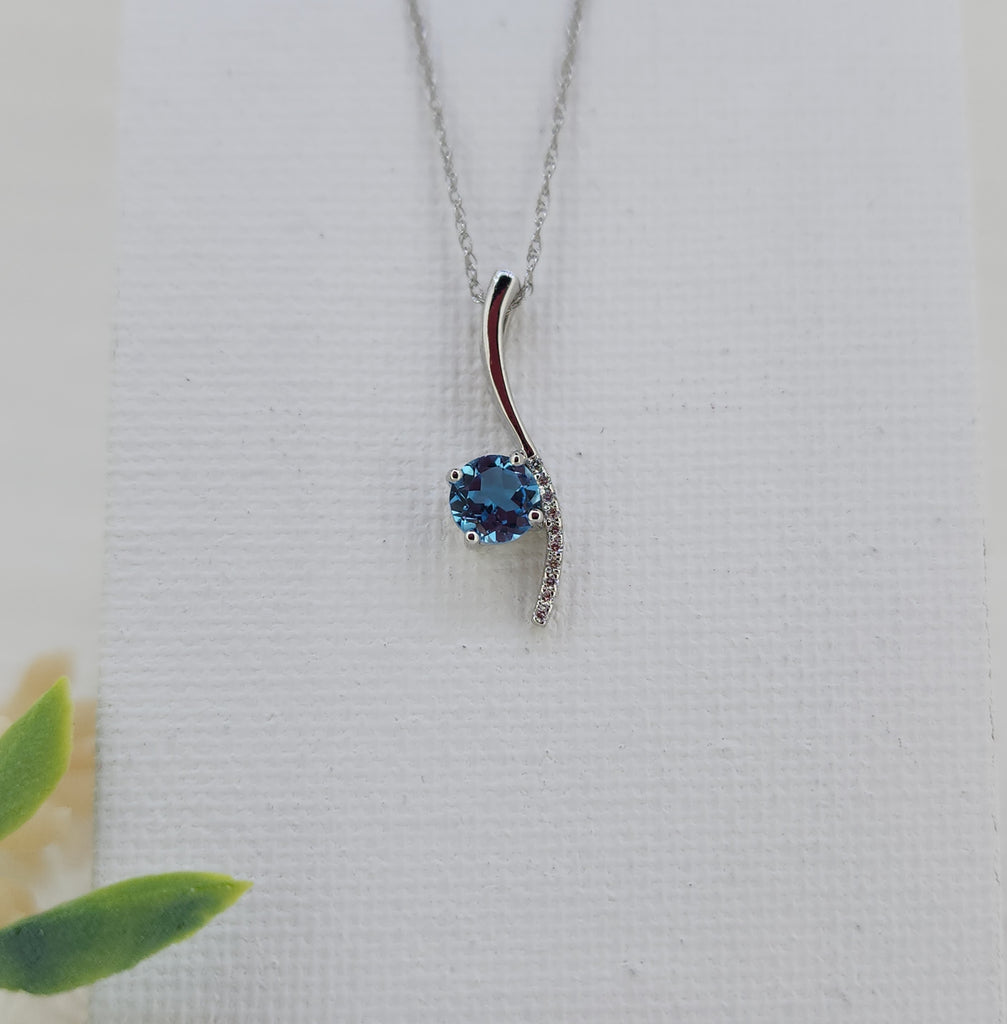 Graceful and modern, this pendant features a 5mm round faceted Swiss blue topaz with vivid color and brilliant sparkle. A curved accent of natural mined round brilliant diamonds totaling .03 carat total weight adds a subtle touch of shimmer and movement.
Crafted in 14K white gold, the pendant measures 19.95mm in length and 5.77mm at its widest point and is suspended from an 18-inch 14K white gold Singapore chain secured with a spring ring clasp. 