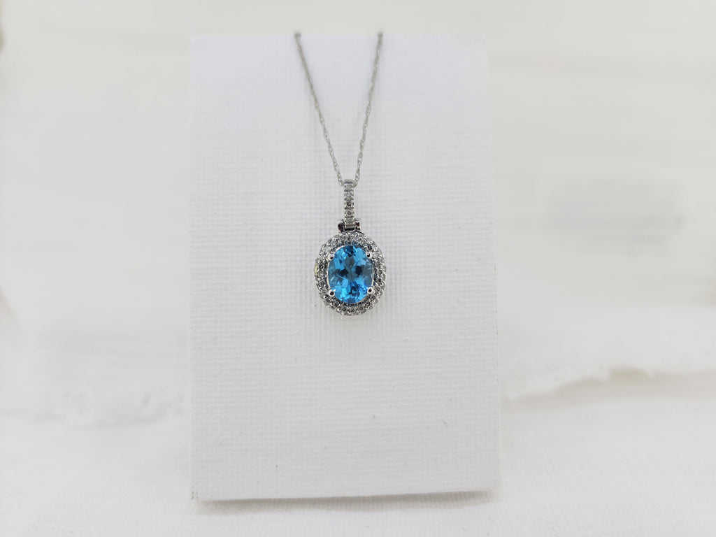 Bold yet refined, this pendant features a 1.76 carat oval Swiss blue topaz with vivid color and luminous clarity. A double halo of natural mined diamonds totaling .36 carat total weight adds layered sparkle and depth to the design.

Crafted in solid 14K white gold, the pendant measures 22.18mm long and 11.53mm wide and is suspended from an 18-inch 14K white gold Singapore chain with a spring ring clasp. A striking statement piece designed to shine!