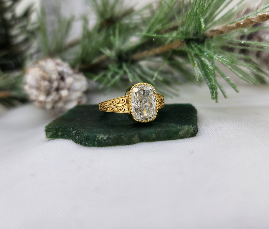 This lovely elongated cushion cut lab diamond ring is made from 14k yellow gold and is set with one 3.04ct lab grown diamond with an IGI report grading of E in color and VS1 in clarity. The milgrain top of the bezel set really adds some nice detail to this already stunning ring!&nbsp;