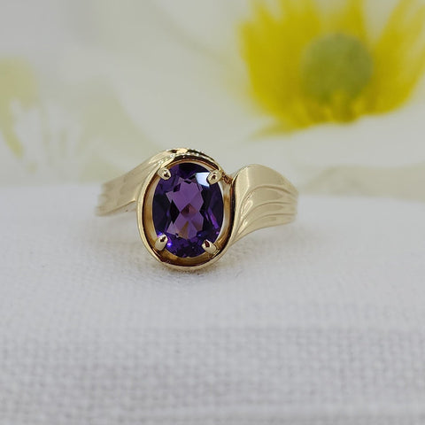 This stunning ring is constructed of 14k yellow gold and is set with an 8x6mm oval natural mined purple amethyst. The ring has a nice modern appeal with a slight twist and ribbed band. The ring measures 10.90mm at the top and tapers to a 1.89mm shank and weighs (including the stone) 4.00 grams.