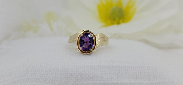 This stunning ring is constructed of 14k yellow gold and is set with an 8x6mm oval natural mined purple amethyst. The ring has a nice modern appeal with a slight twist and ribbed band. The ring measures 10.90mm at the top and tapers to a 1.89mm shank and weighs (including the stone) 4.00 grams.