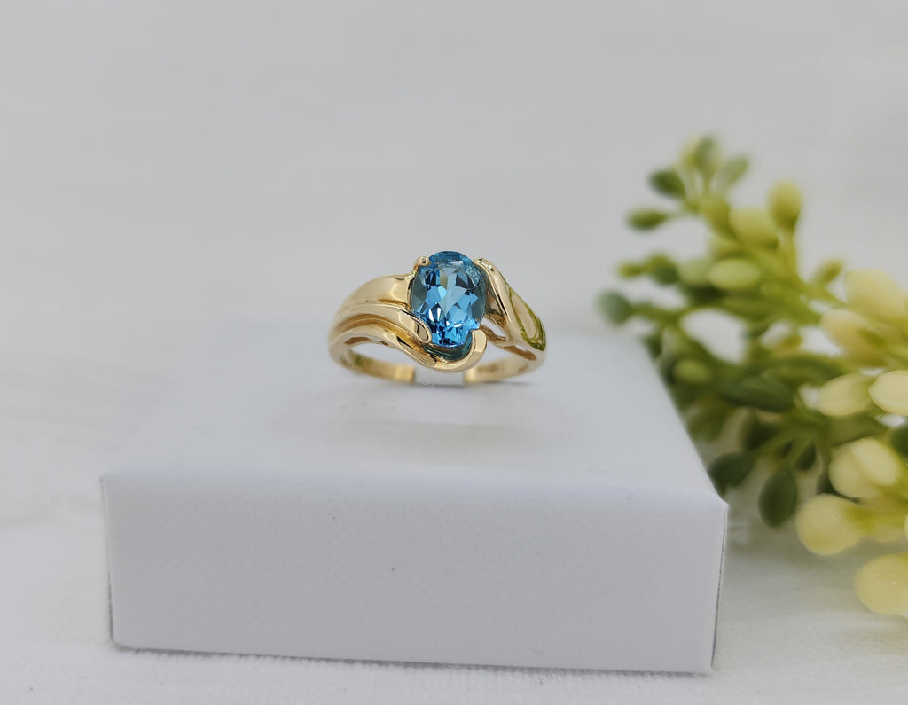 Modern and effortlessly wearable, this ring features a 7.91 × 5.85mm oval Swiss blue topaz, showcasing vivid color and elegant faceting. The gemstone is set in a sleek 14K yellow gold design with smooth, sculptural lines that create a contemporary look.

Designed with a low-profile setting, the ring measures 9.62mm across the top and tapers to a slender 1.79mm shank, offering both comfort and everyday versatility. With a total weight of 3.6 grams including the stone, this piece balances modern style with a 