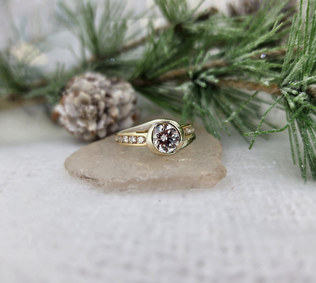 This lovely ring is constructed of 14K yellow and 14K white gold. In addition to the blend of metal color, the ring is set with a 1.00ct round brilliant cut LAB grown diamond as the center (D color, VS1 clarity EX cut, polish, symmetry) In addition to the center diamond is .45cttw in round brilliant cut natural mined diamonds, five channel set on each side of the bezel set center diamond. The ring measures 9mm at the top and tapers to a 2.37mm shank. Finger size USA 7.50