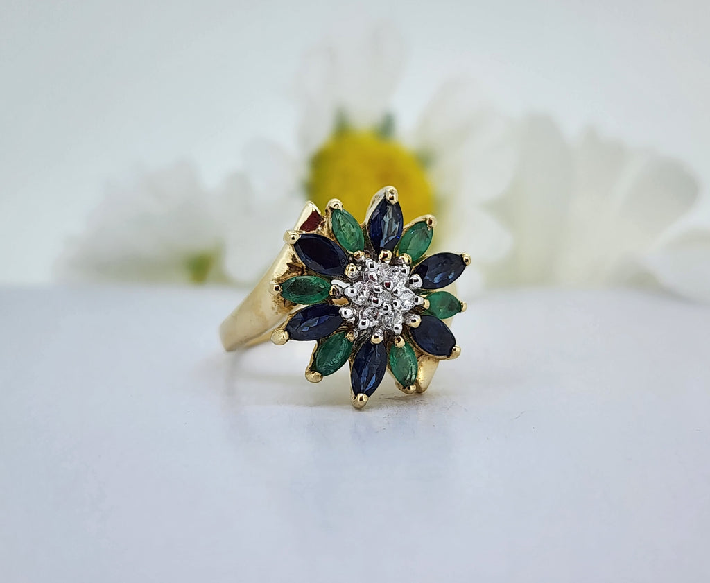 For all you nature lovers out there, is this stunning 14k yellow gold flower ring set with 4.50mmx2.50mm alternating natural Sapphires and Emeralds. In the center of the flower are seven single cut natural mined diamonds. The ring measures 15.87mm across the top and tapers to a 2.10mm shank. The ring weighs 4.40 grams
