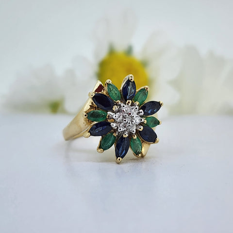 For all you nature lovers out there, is this stunning 14k yellow gold flower ring set with 4.50mmx2.50mm alternating natural Sapphires and Emeralds. In the center of the flower are seven single cut natural mined diamonds. The ring measures 15.87mm across the top and tapers to a 2.10mm shank. The ring weighs 4.40 grams