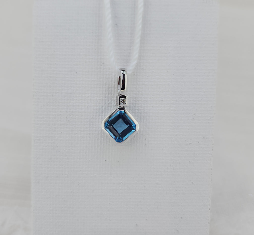 Crisp and contemporary, this pendant features a 6×6mm square step-cut Swiss blue topaz, admired it's clean, architectural facets. A subtle .01 carat natural mined round brilliant diamond accent adds a delicate touch of sparkle, enhancing the design .
Crafted in 14K white gold, the sleek setting highlights the topaz’s striking color and geometric form. Sold without a chain 