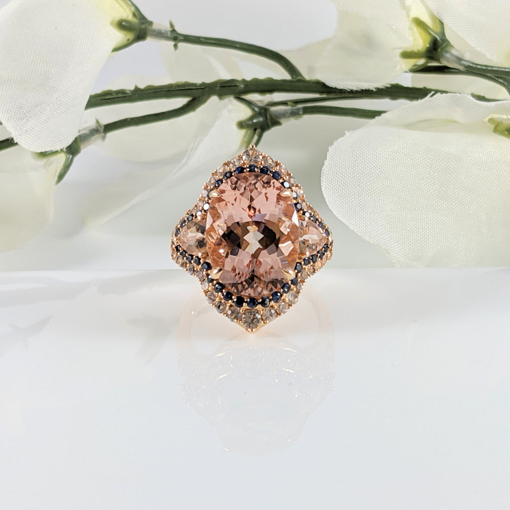 The unique color combination of the kiss of pink from the  Morganite against the deep blue of Sapphires is a stunning contrast in this ring. The Morganite is just over 4.00cts. The White Sapphires give a shimmer effect drawing your eye immediately to this beautiful ring. This ring is for those that like a big look, measuring 25mm in length. Absolutely fabulous! Constructed of 14K rose gold. Finger size 8  $1525.00