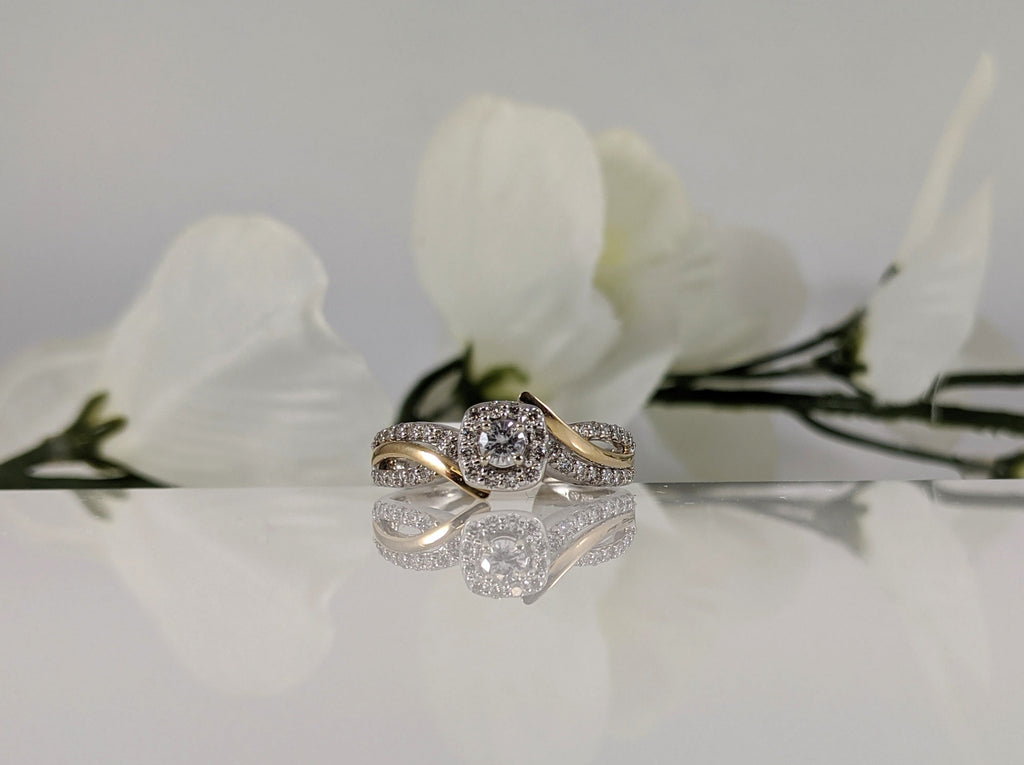 10 k white and yellow gold diamond engagement ring featuring a .15ct round brilliant cut center diamond. This ring features and additional .22cttw in accent diamonds in a bypass design. Finger size 7. $1400.00